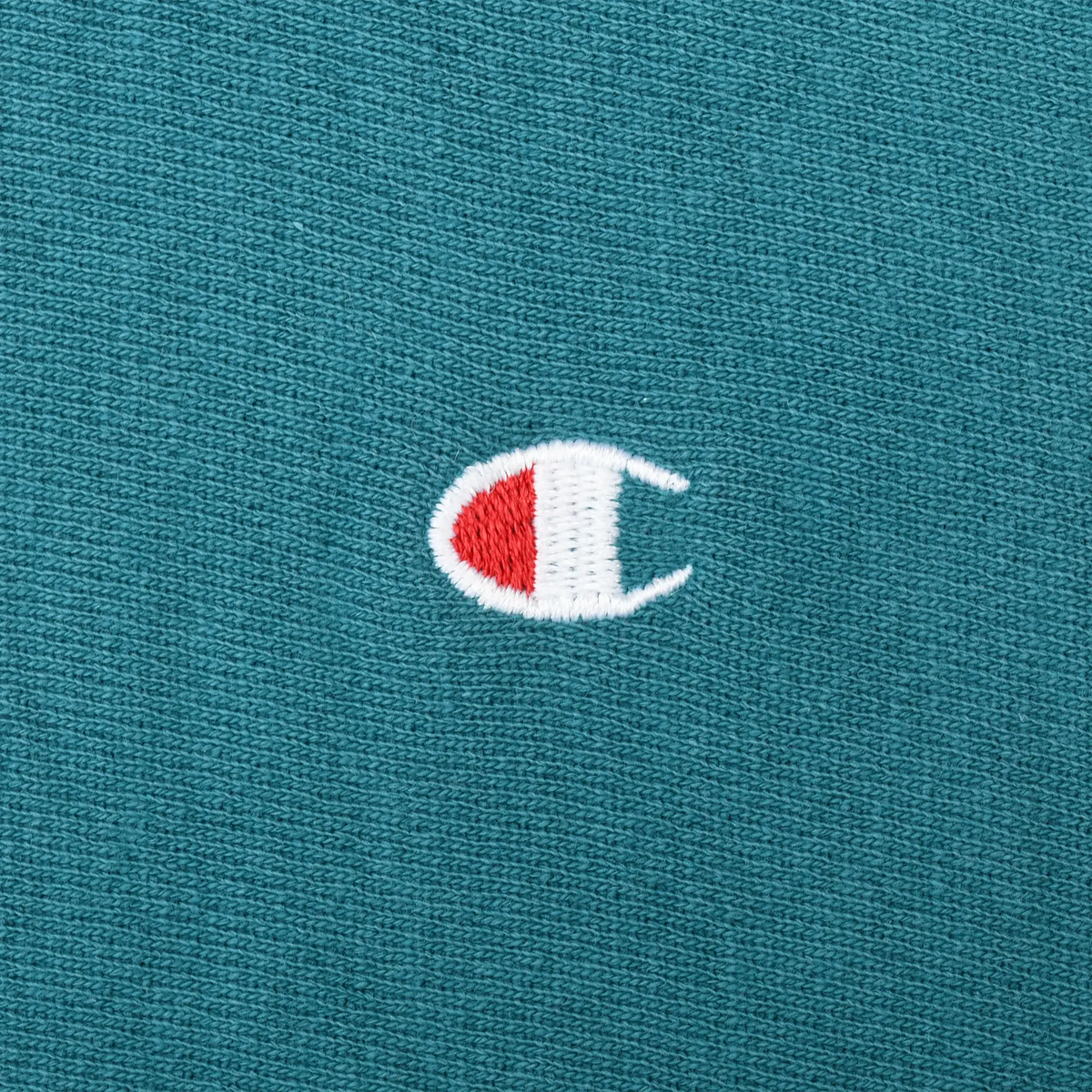Close-up of red and white Champion logo embroidery on teal sweatshirt chest