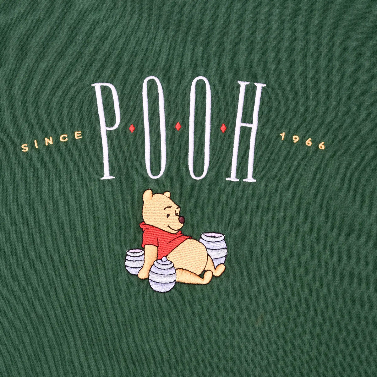 Close-up of embroidered Pooh chest graphic with Winnie the Pooh sitting among honey pots