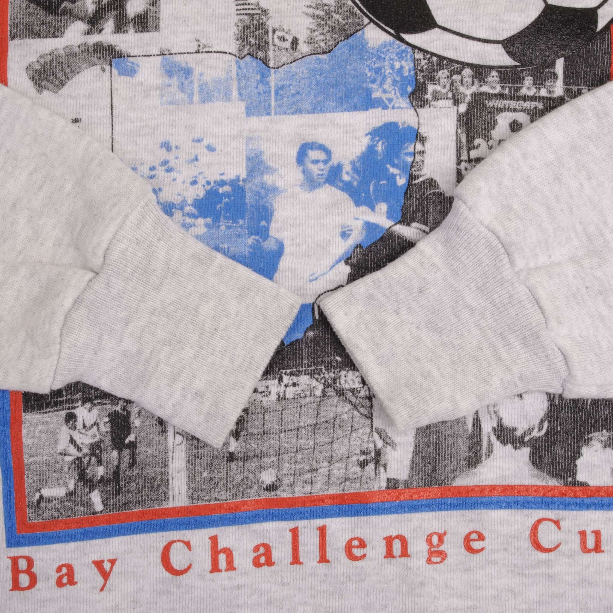Gray sweatshirt cuff detail over Bay Challenge Cup soccer graphic