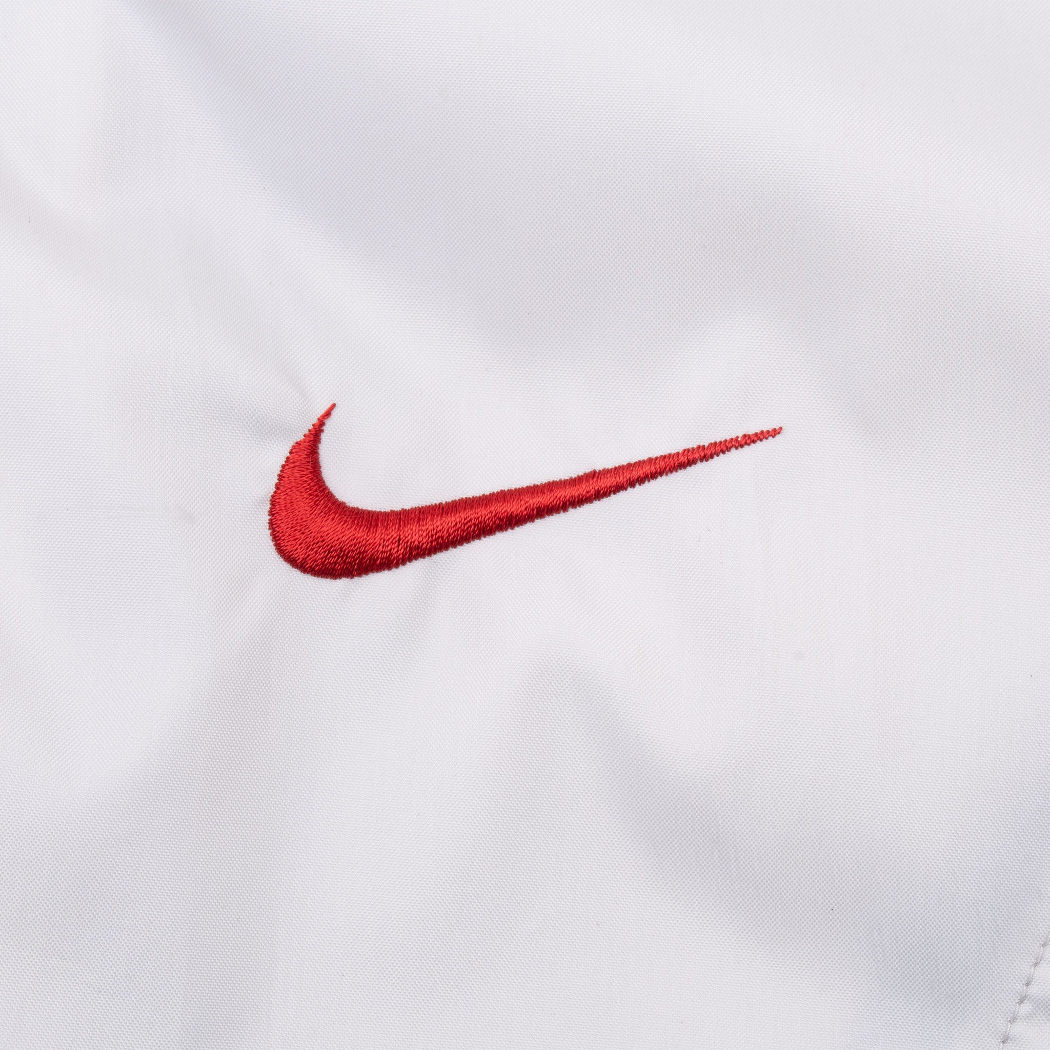 Close-up of small red embroidered Nike Swoosh on white chest fabric