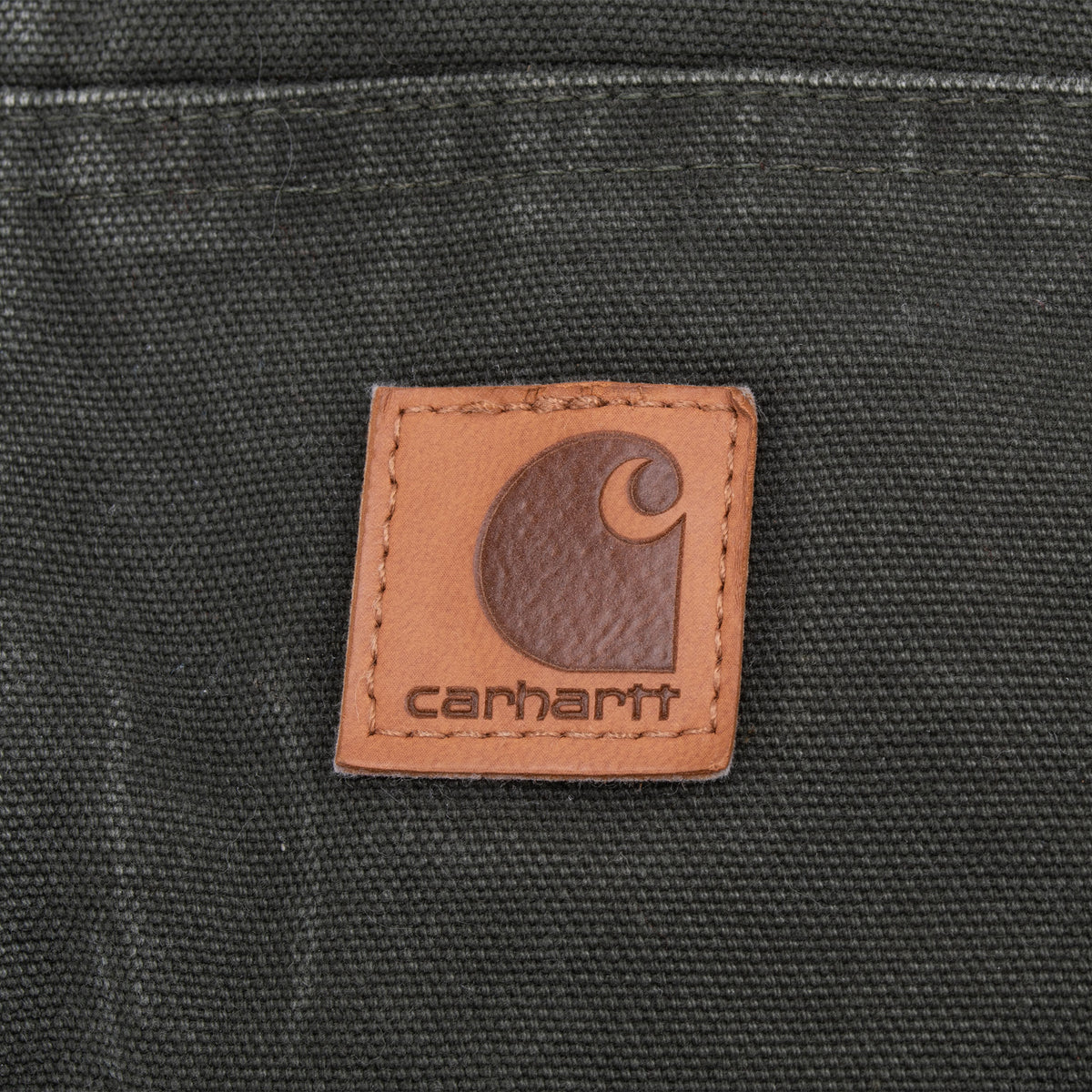 Close-up of brown Carhartt logo patch stitched to the moss green front pocket