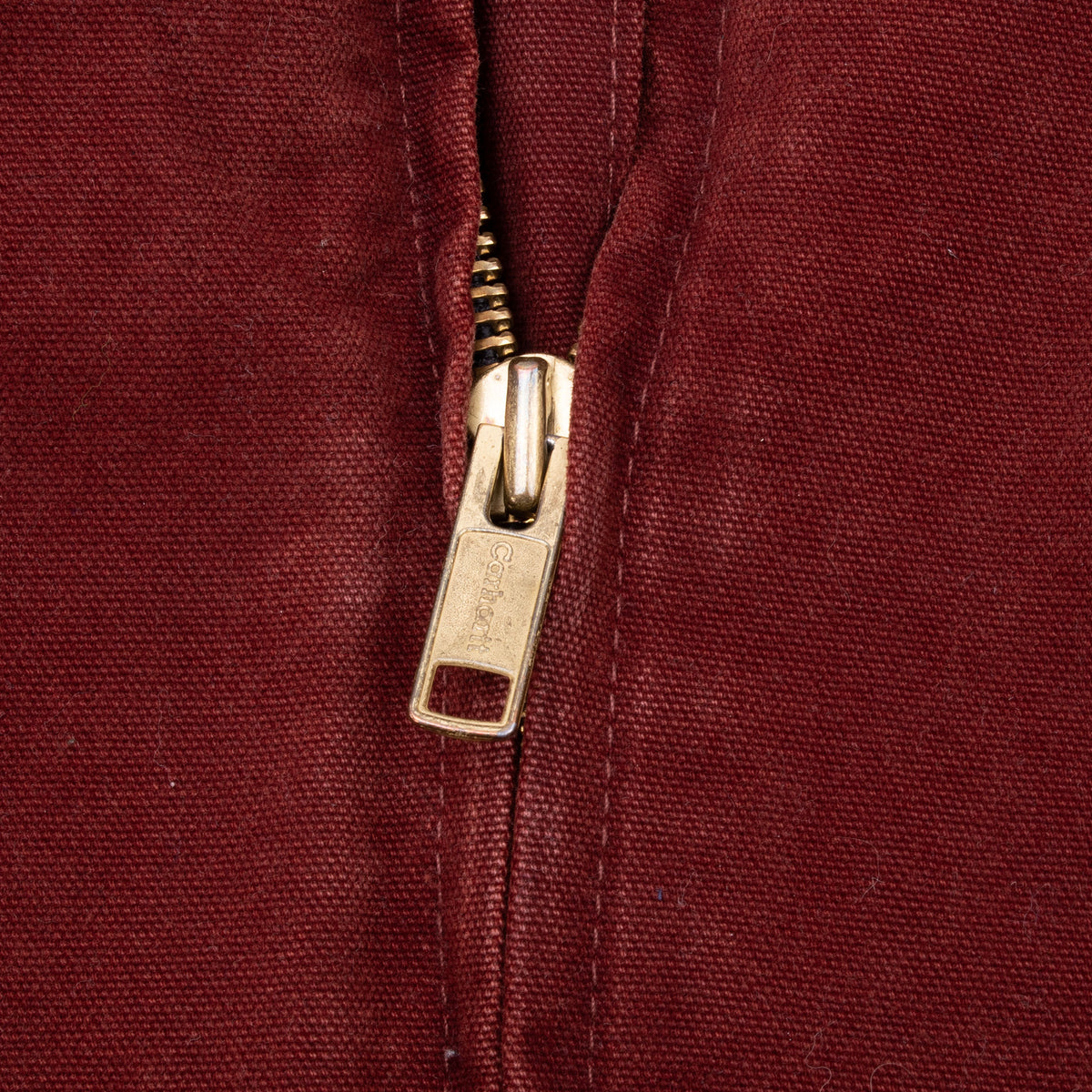 Close-up of brass Carhartt zipper pull on clay red jacket