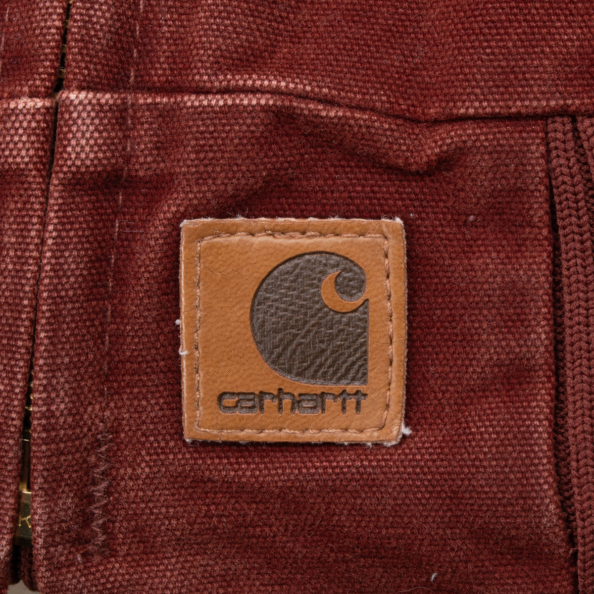 Close-up of Carhartt logo patch near the clay red jacket hem