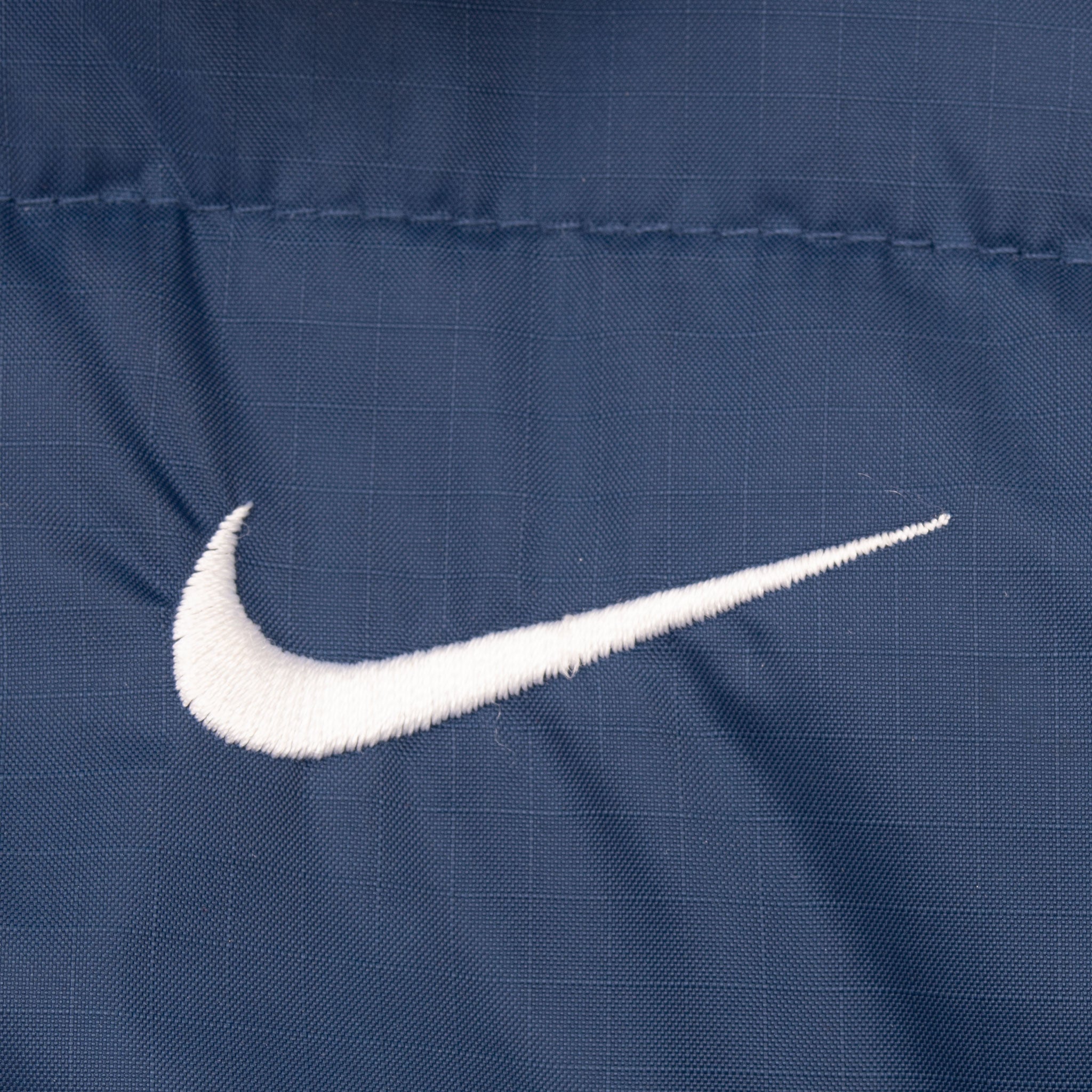 Close-up of white embroidered Nike Swoosh on blue jacket fabric