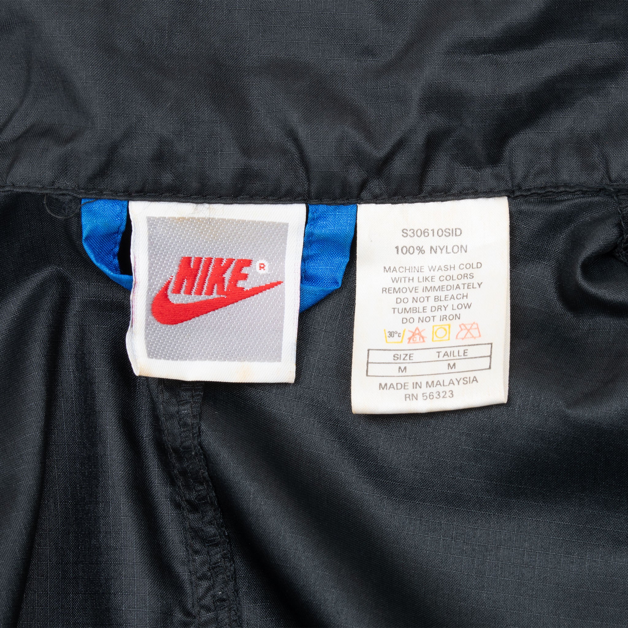 Nike neck label and medium care tag inside black windbreaker