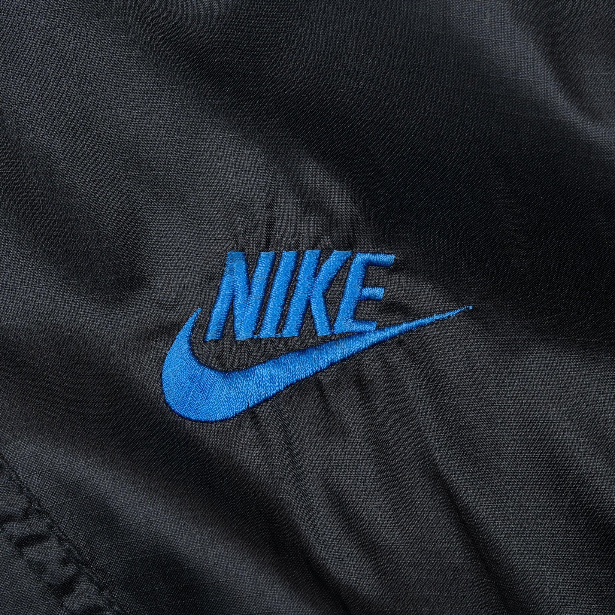 Close-up of bright blue Nike Swoosh embroidery on black windbreaker chest