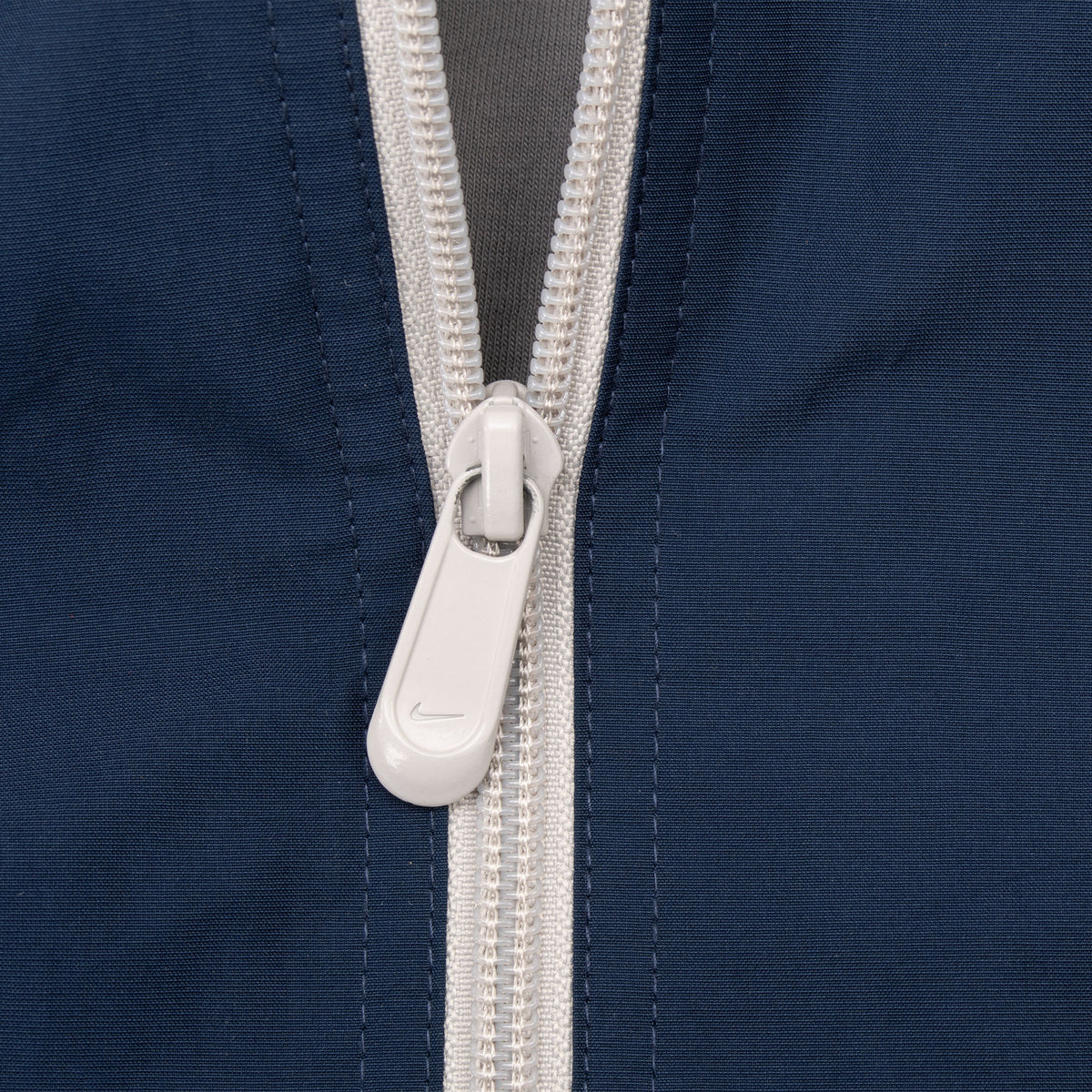 Close-up of white front zipper and Nike-branded pull on navy windbreaker