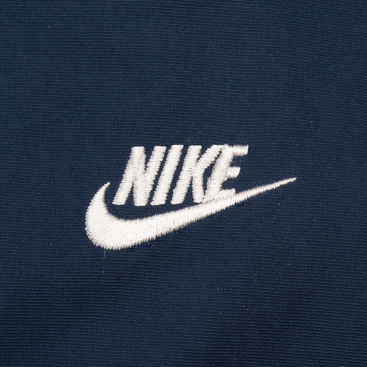 Close-up of white embroidered Nike Swoosh logo on navy fabric