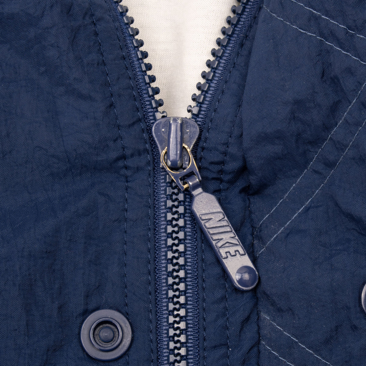 Close-up of Nike-branded zipper pull and snap-secured storm flap on blue windbreaker