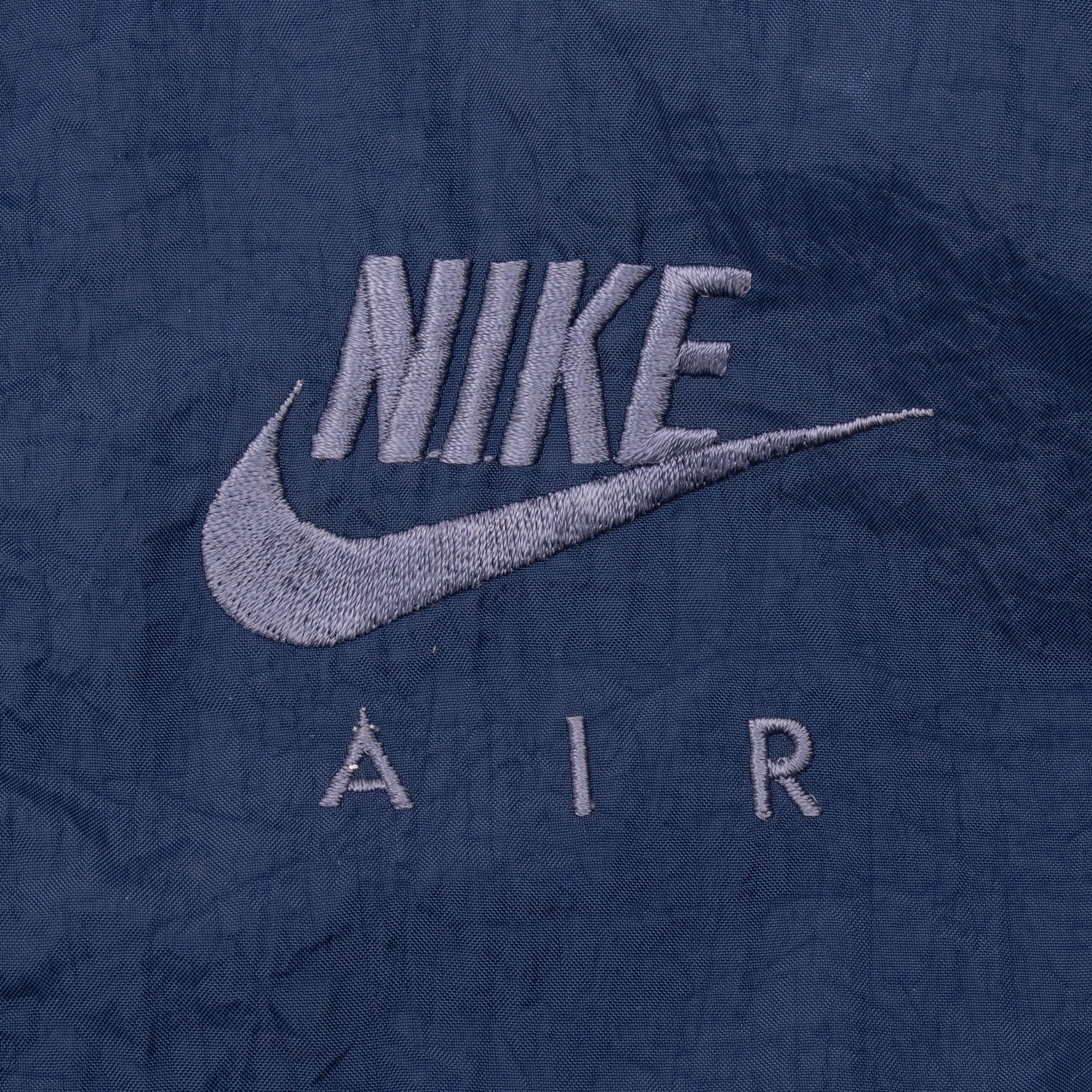 Close-up of gray embroidered Nike Air Swoosh logo on blue windbreaker chest