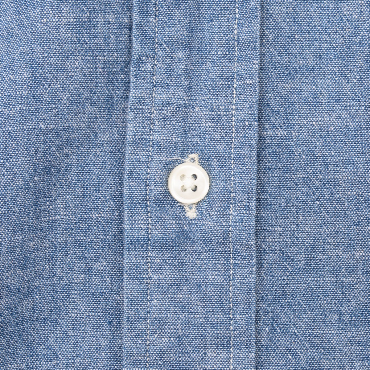 Close-up of white four-hole front button and stitching on blue chambray shirt
