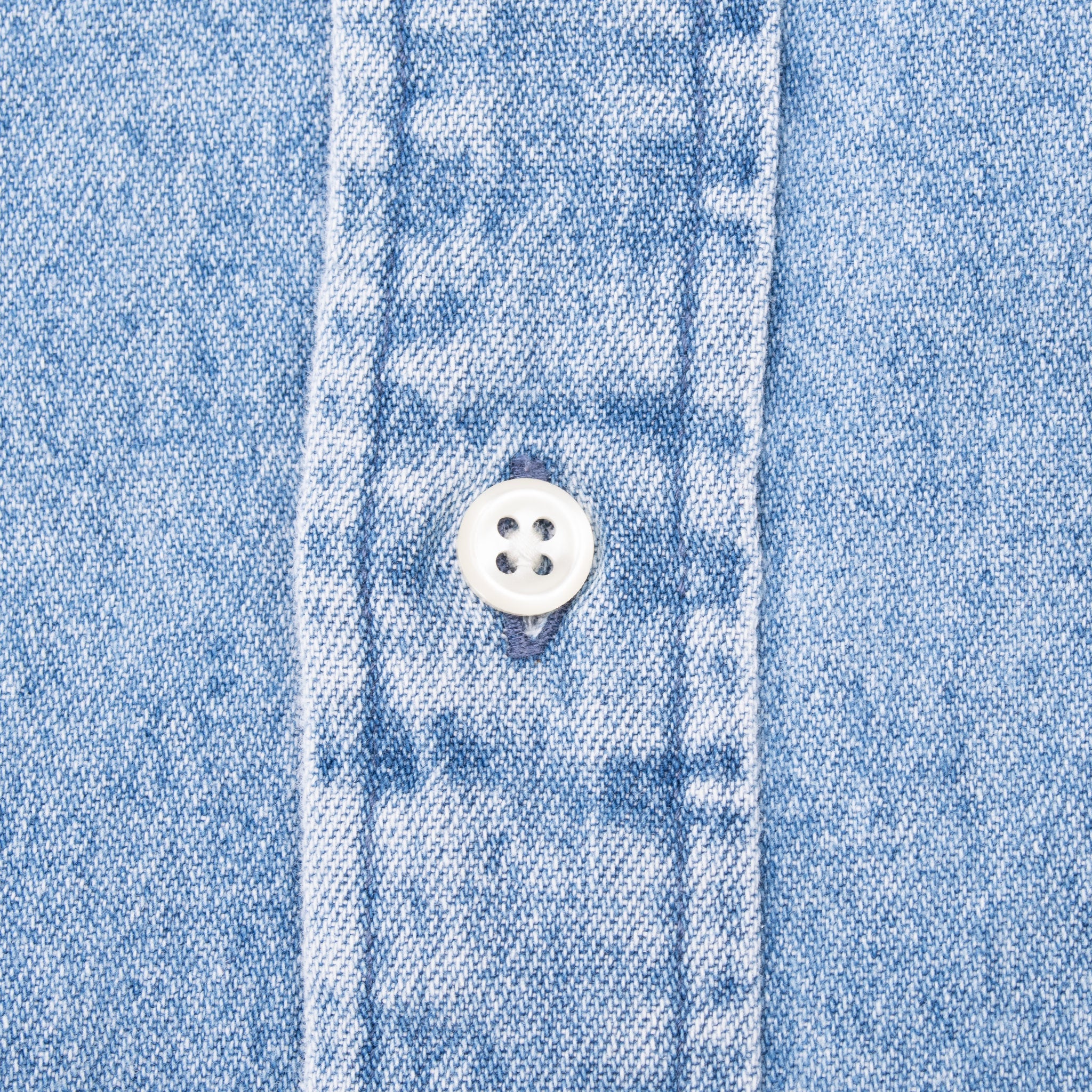 Close-up of white four-hole button and stitching on blue denim shirt placket