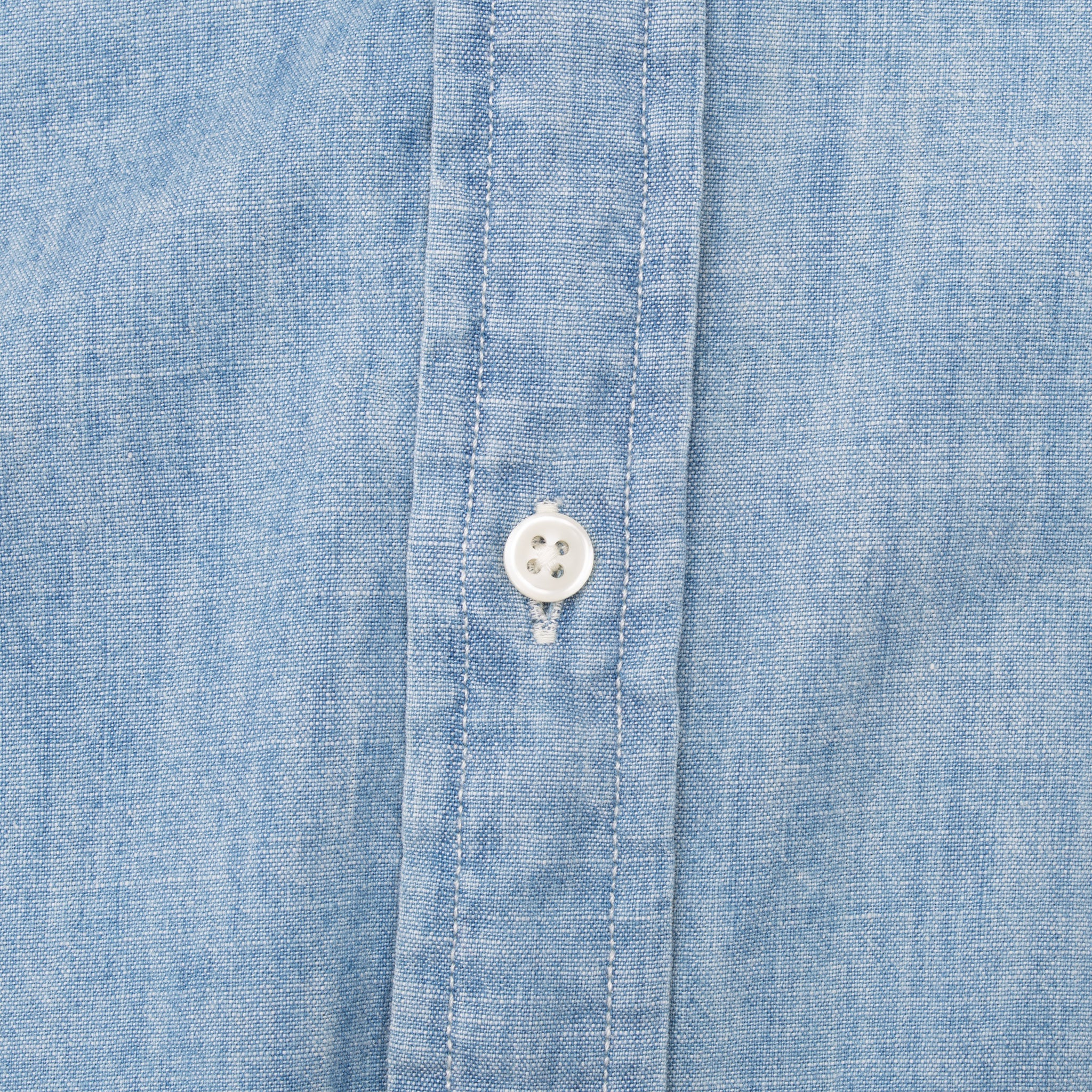 Close-up of white button, stitching, and placket on blue chambray shirt