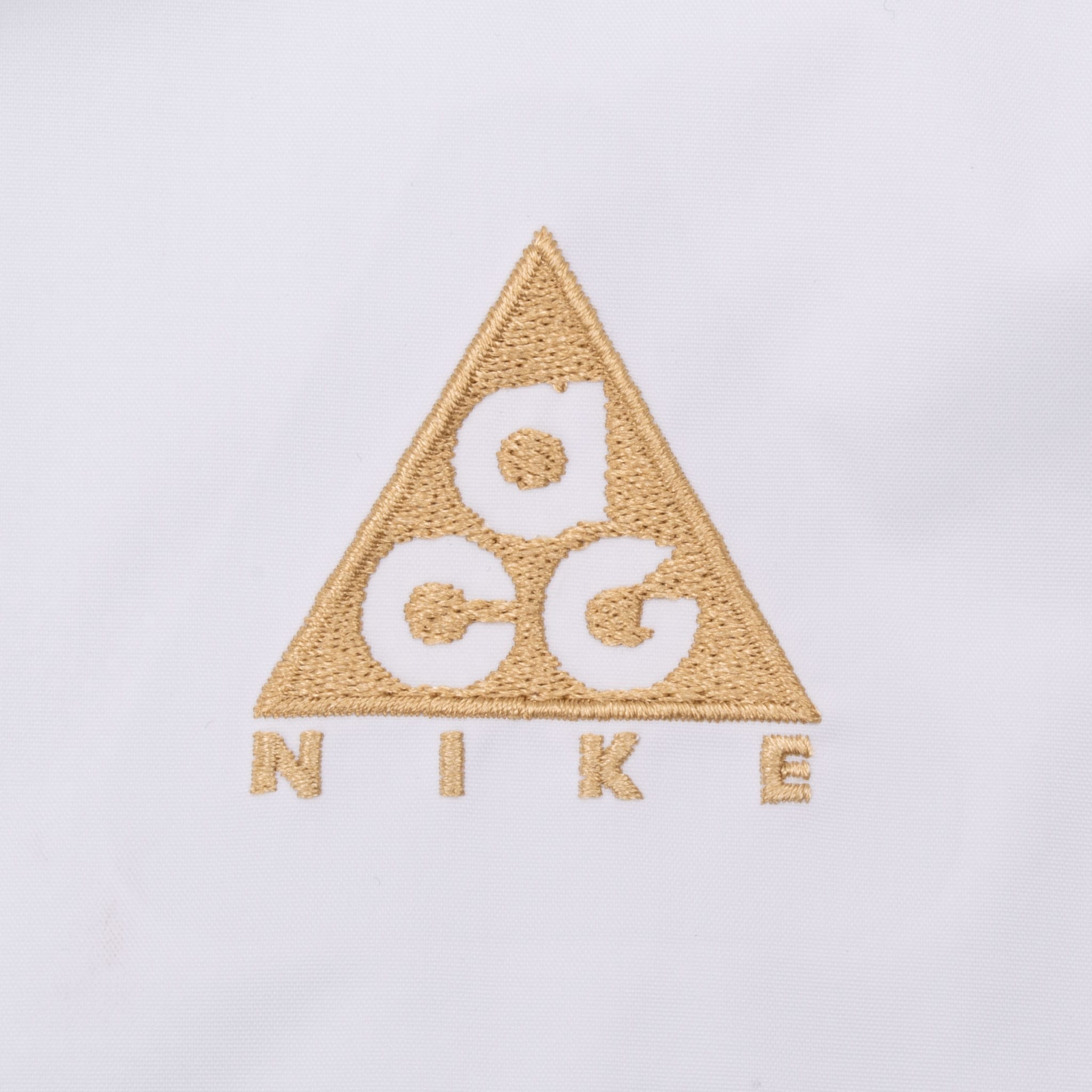 Close-up of tan embroidered Nike ACG logo on white fabric