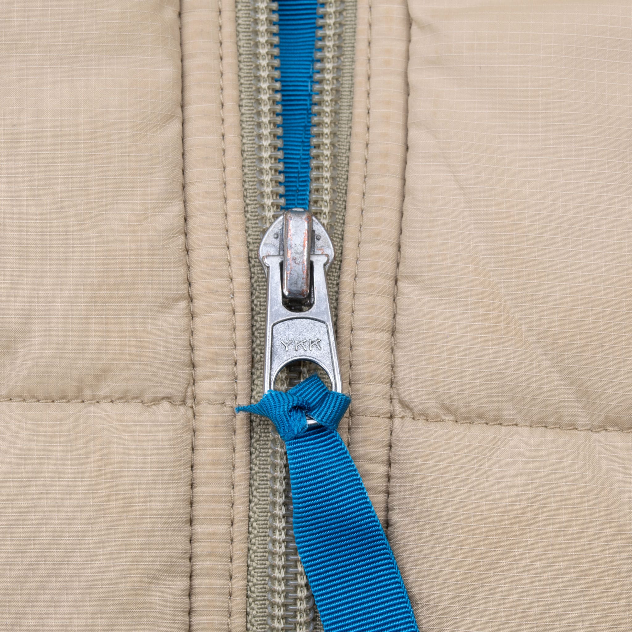 Close-up of YKK front zipper with bright blue pull on beige quilted fabric