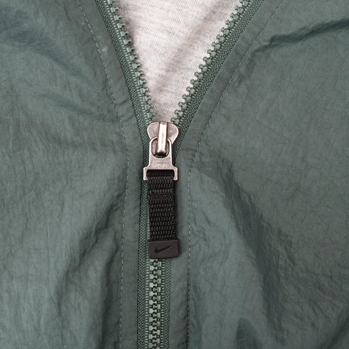 Close-up of green front zipper with black Nike Swoosh pull tab