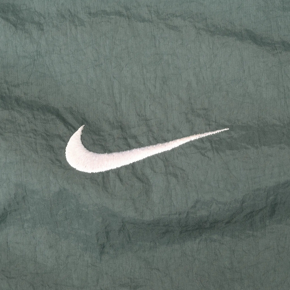 Close-up of white Nike Swoosh embroidery on green jacket fabric