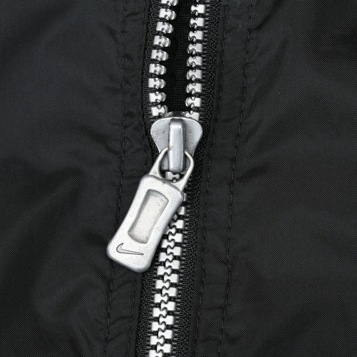 Close-up of silver front zipper and Nike Swoosh pull on black fabric