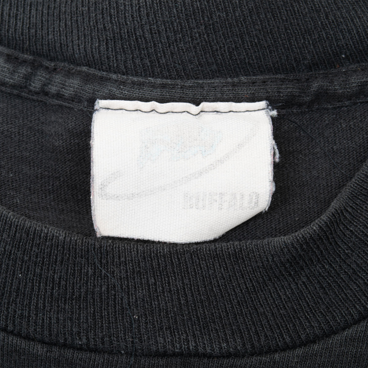 Close-up of faded white neck tag and ribbed collar on black T-shirt