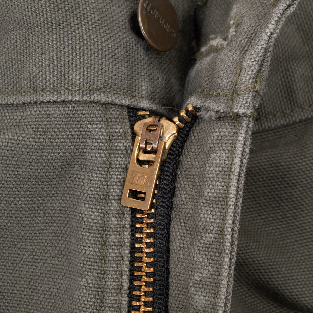 Close-up of brass-tone zip fly and Carhartt button on green carpenter pants