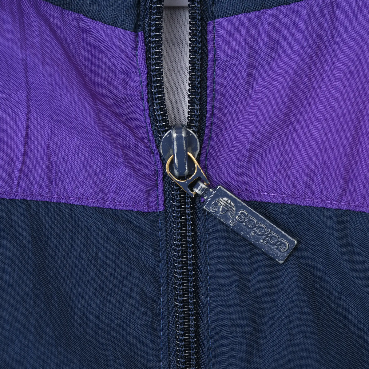 Close-up of Adidas-branded zipper pull on the purple and navy windbreaker