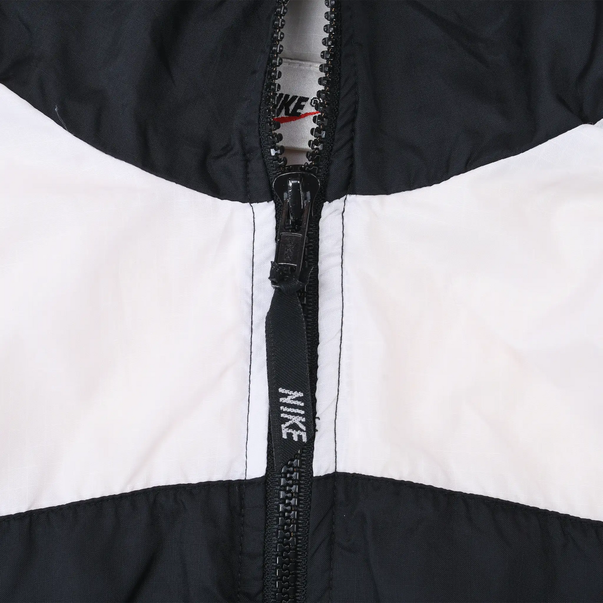 Close-up of black front zipper and Nike-branded zipper pull on white and black panels