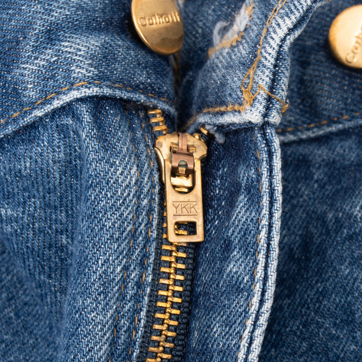 Close-up of YKK zip fly and Carhartt-branded hardware on blue jeans