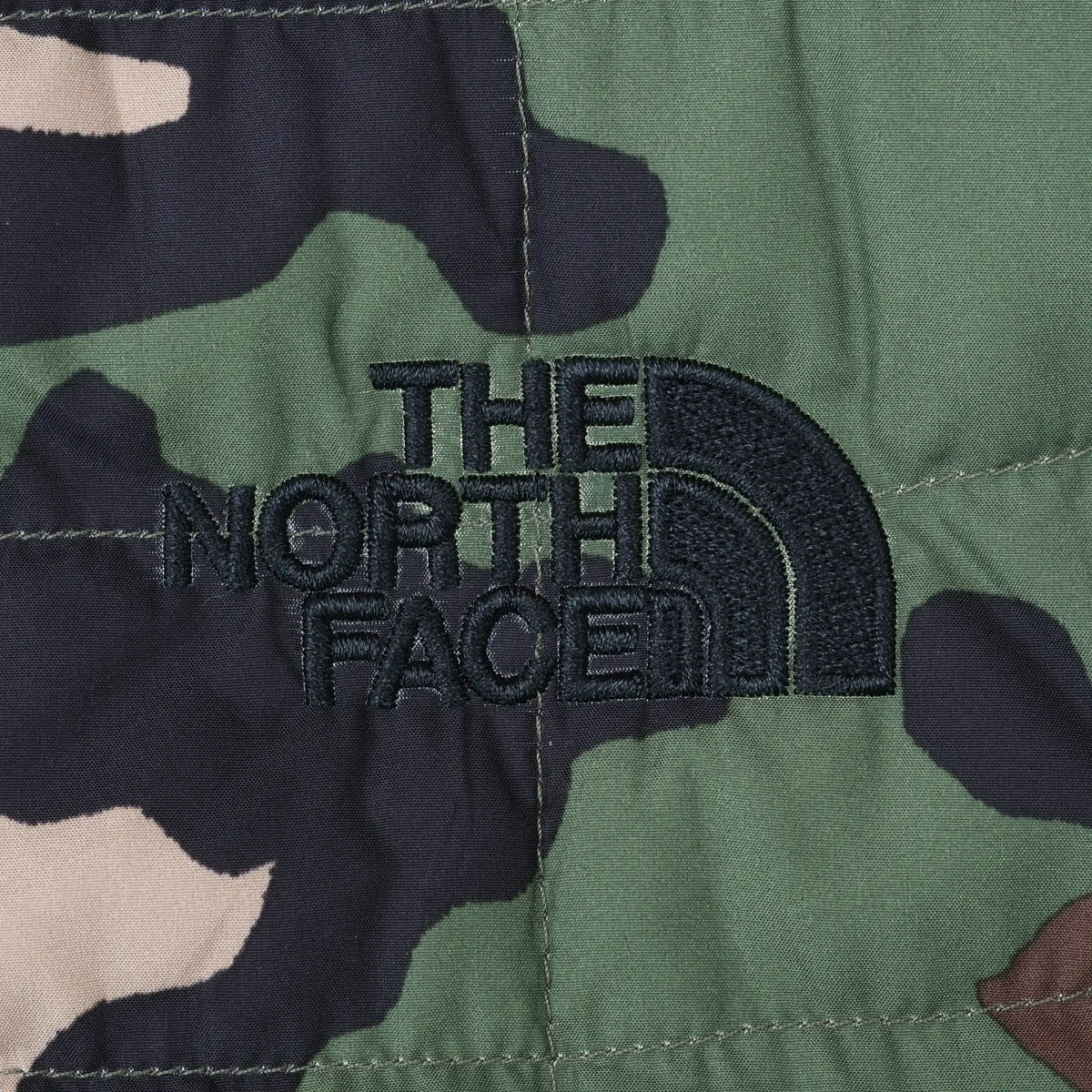 Close-up of black The North Face logo embroidery on green camouflage quilted fabric