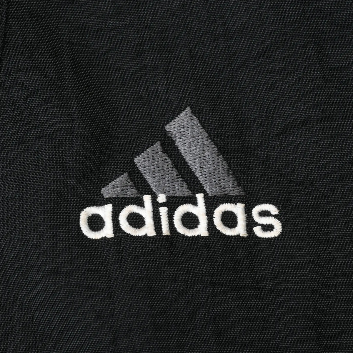 Close-up of gray and white Adidas chest logo embroidery on black fabric