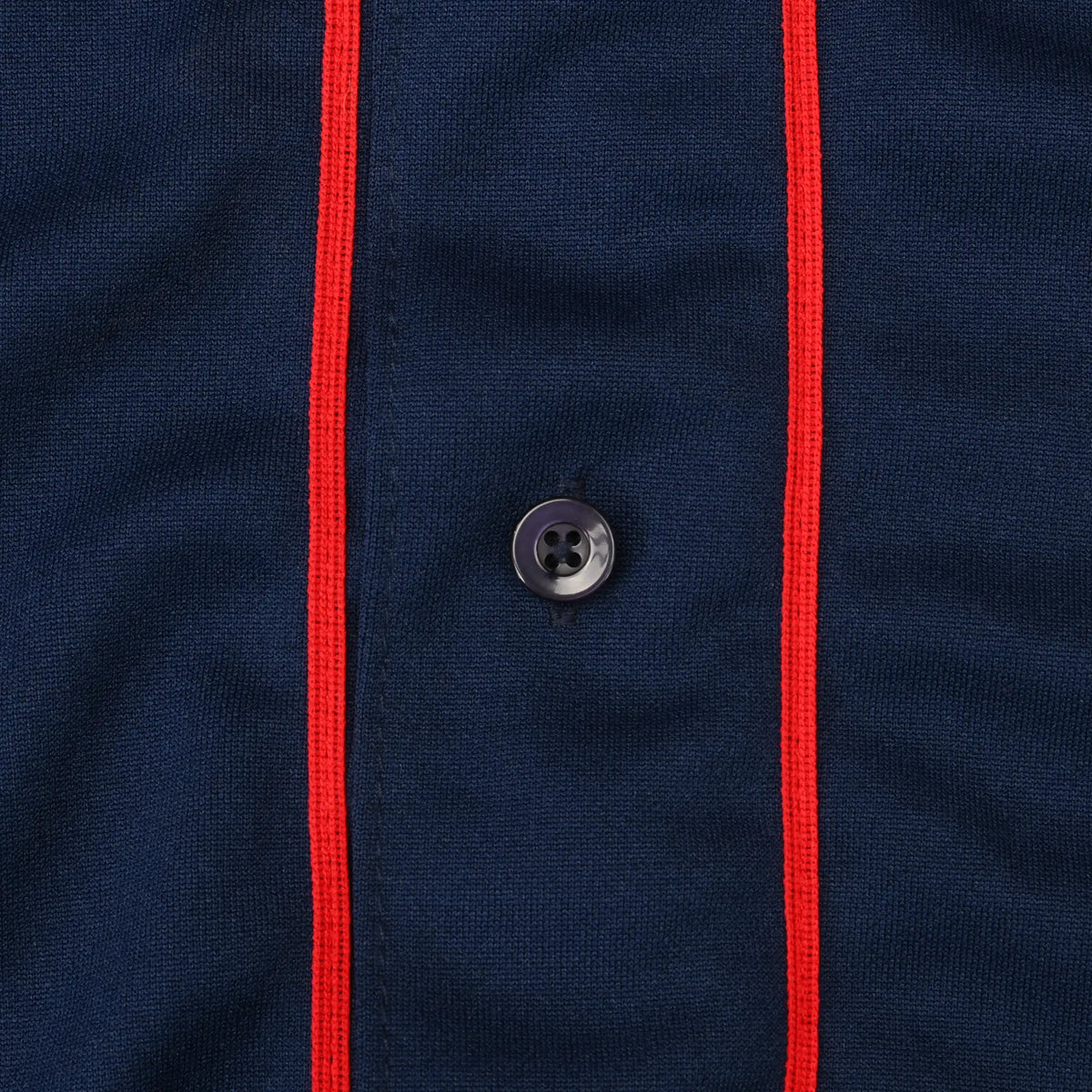 Close-up of black jersey button between red piping on navy fabric