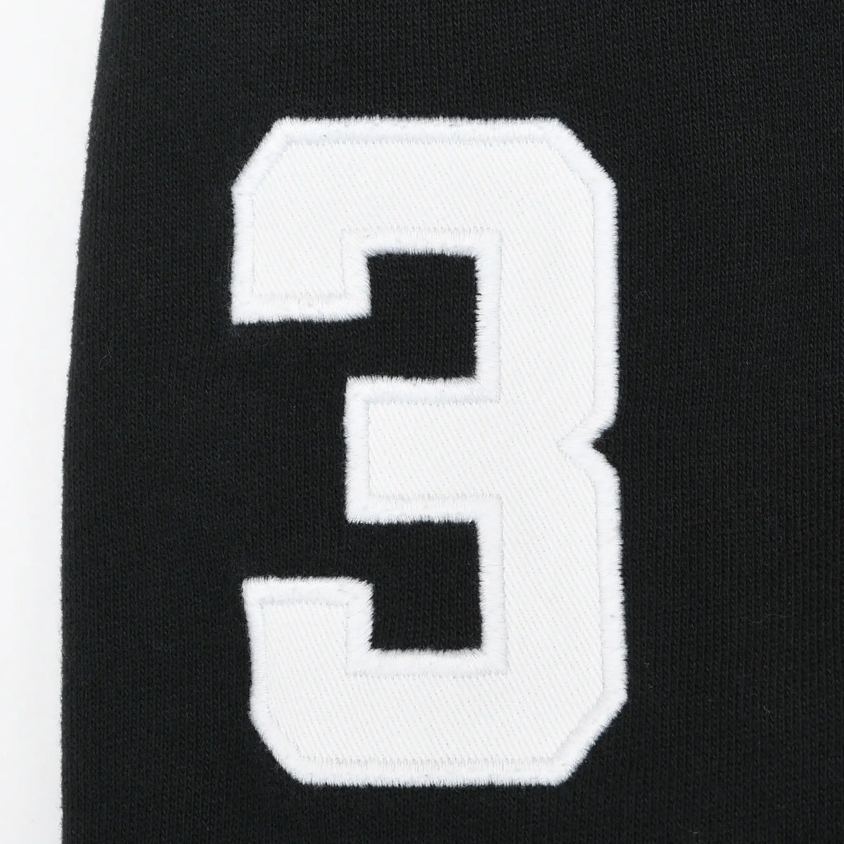 Close-up of white embroidered number 3 patch on black hoodie sleeve