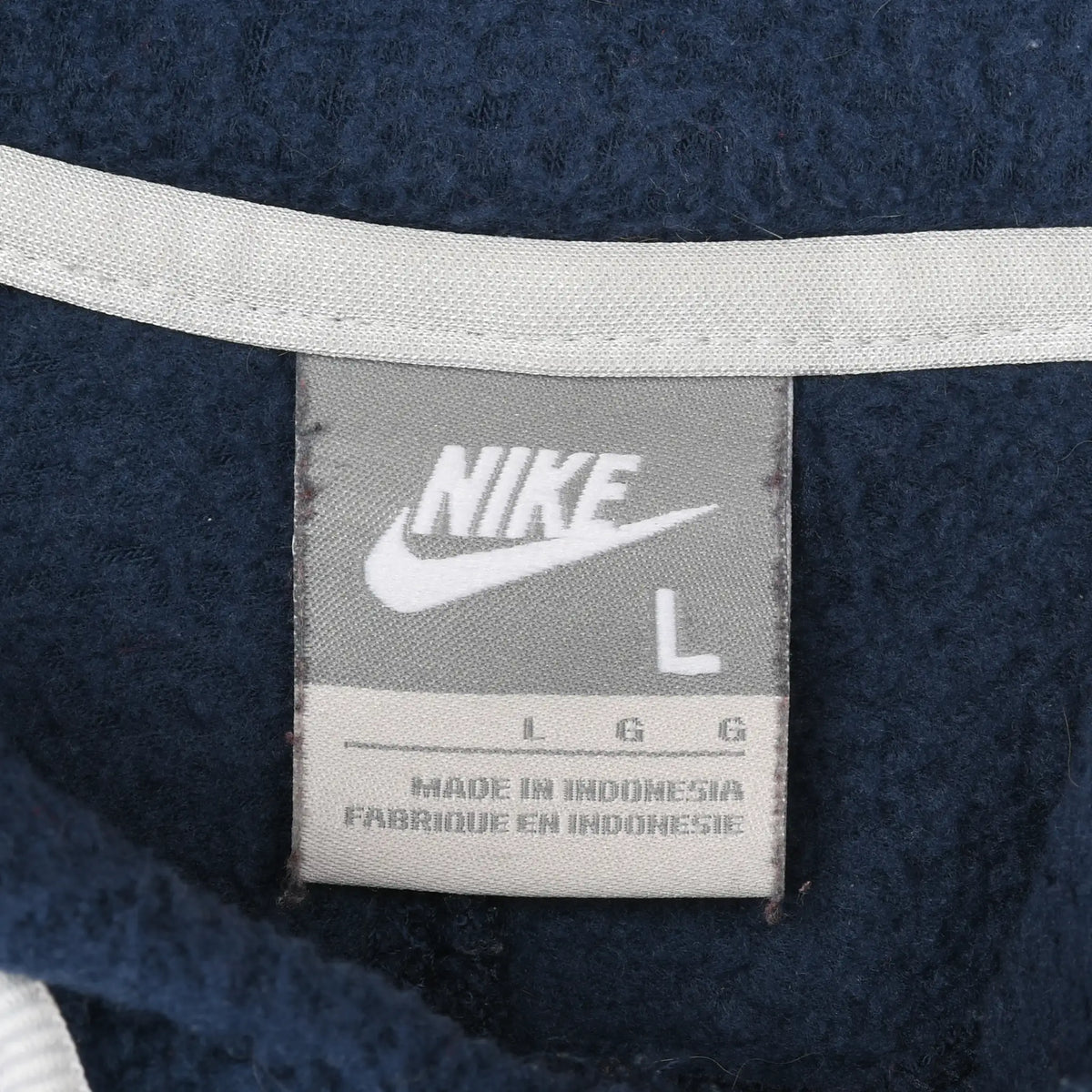 Close-up of gray Nike neck label marked size L inside navy fleece hoodie