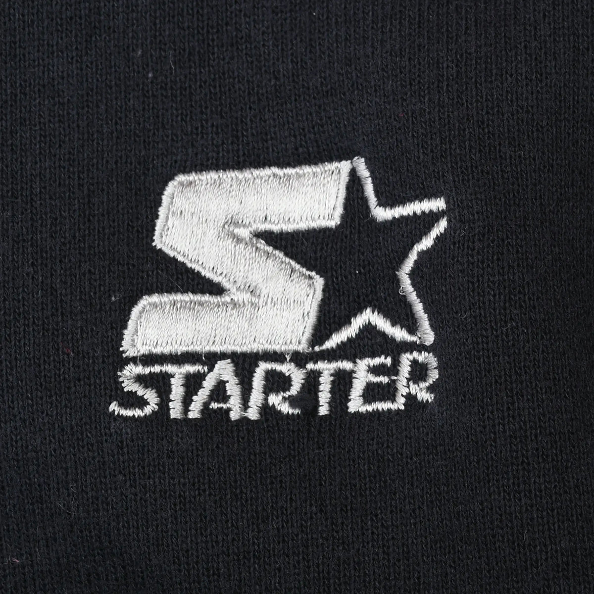 Close-up of white Starter logo embroidery on black sweatshirt fabric