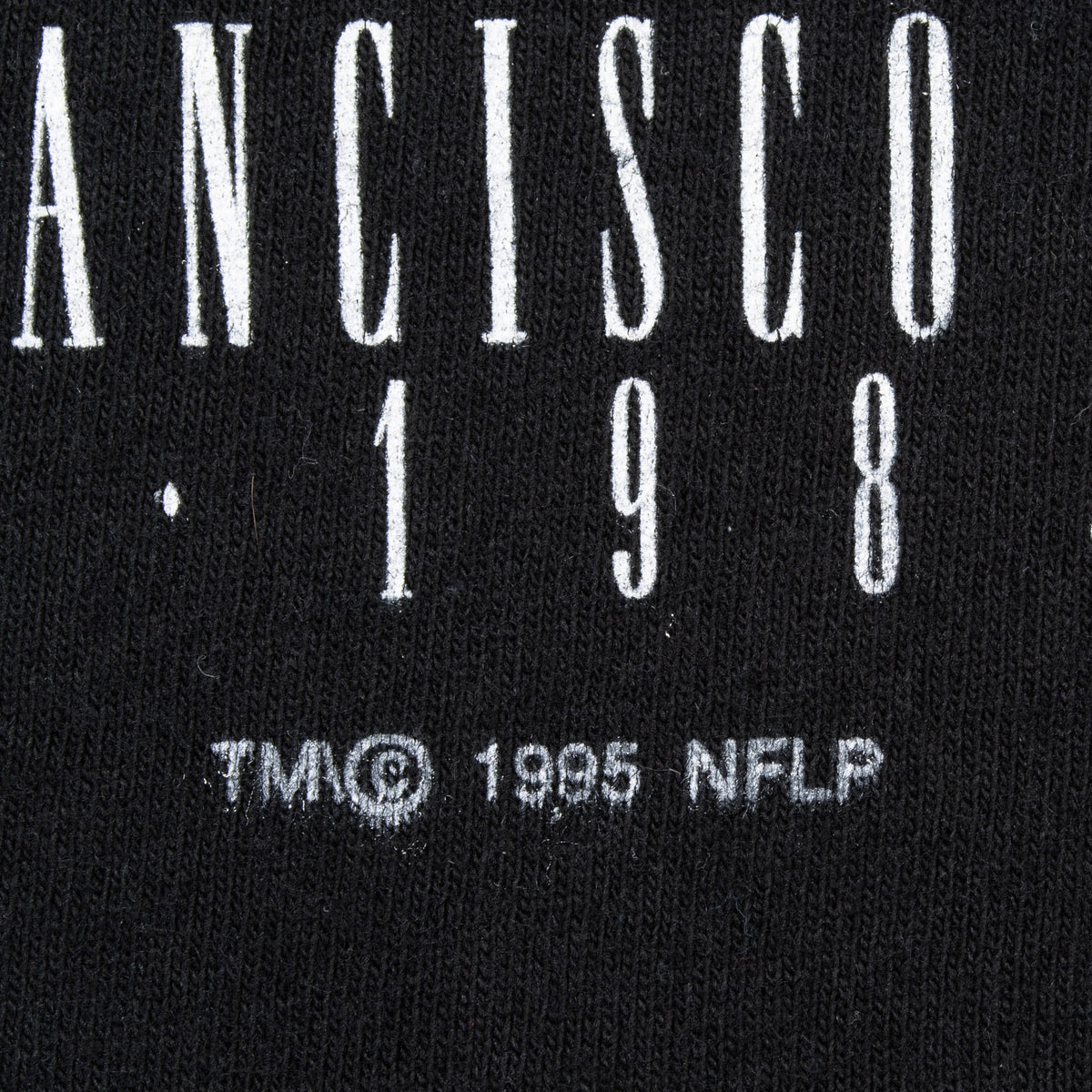Close-up of white graphic text and TM © 1995 NFLP marking on black fabric