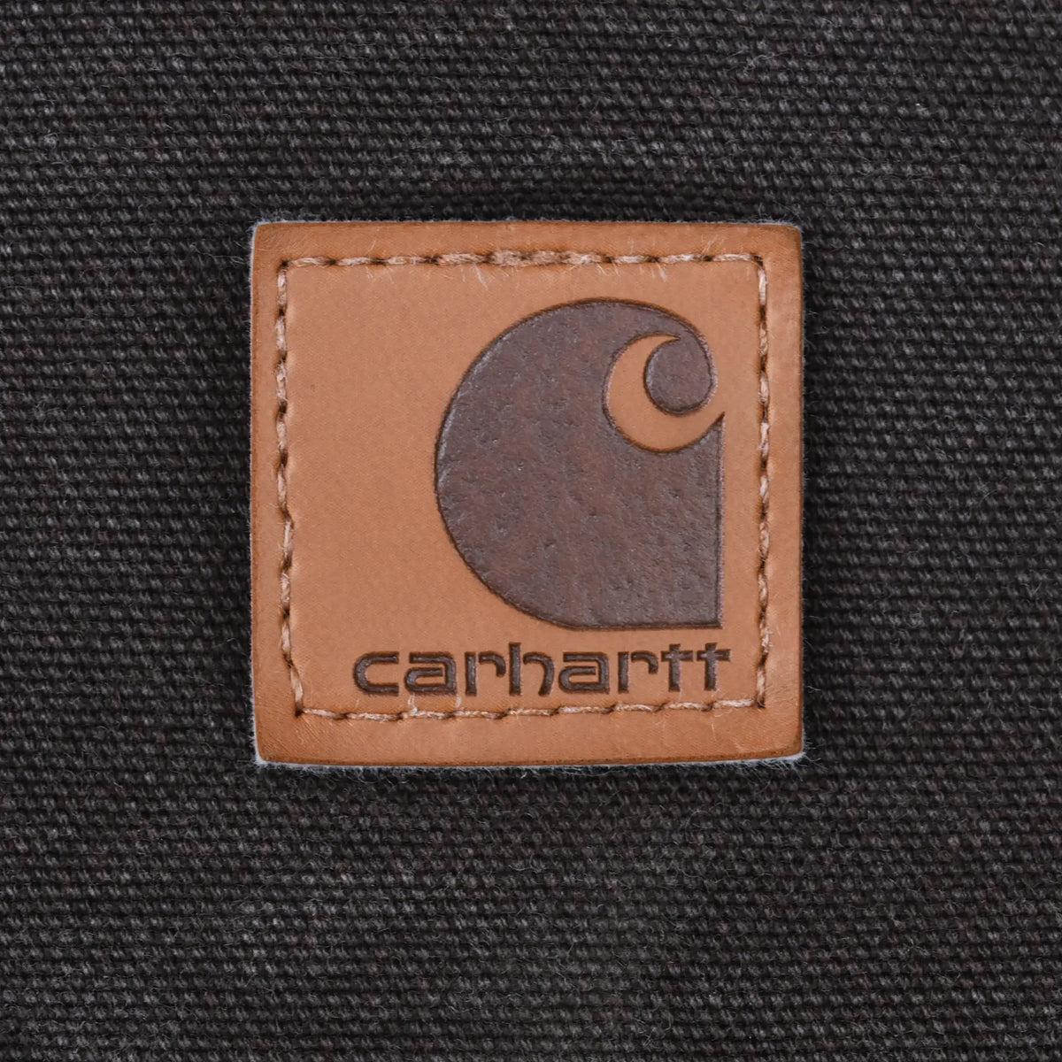 Close-up of tan Carhartt logo patch stitched onto dark brown fabric