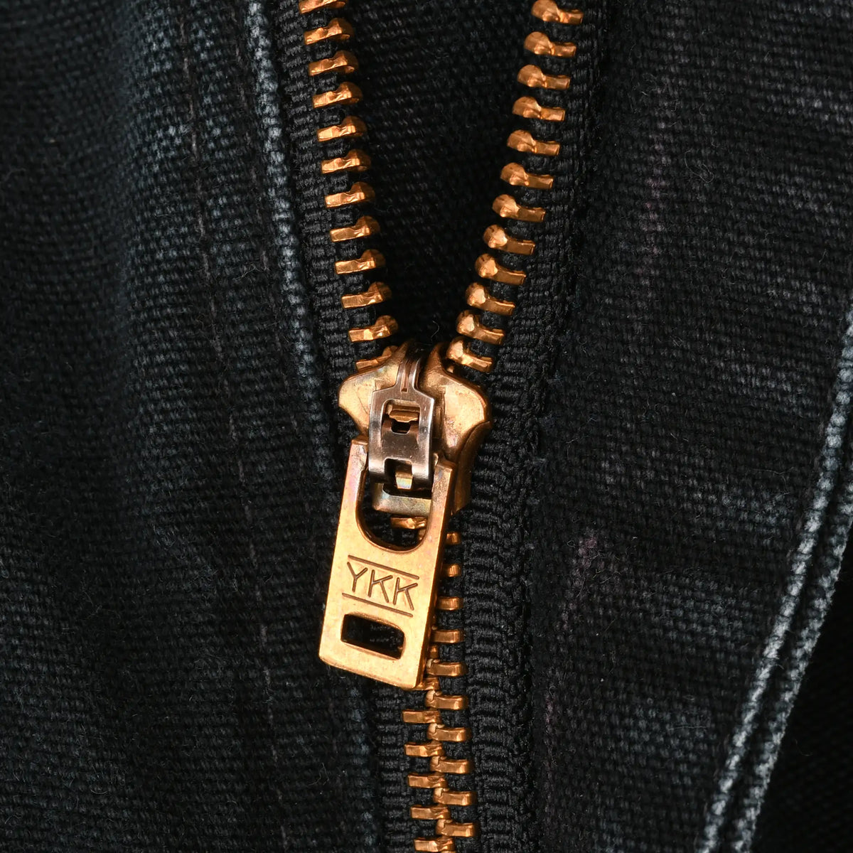 Close-up of brass YKK zipper on black Carhartt pants