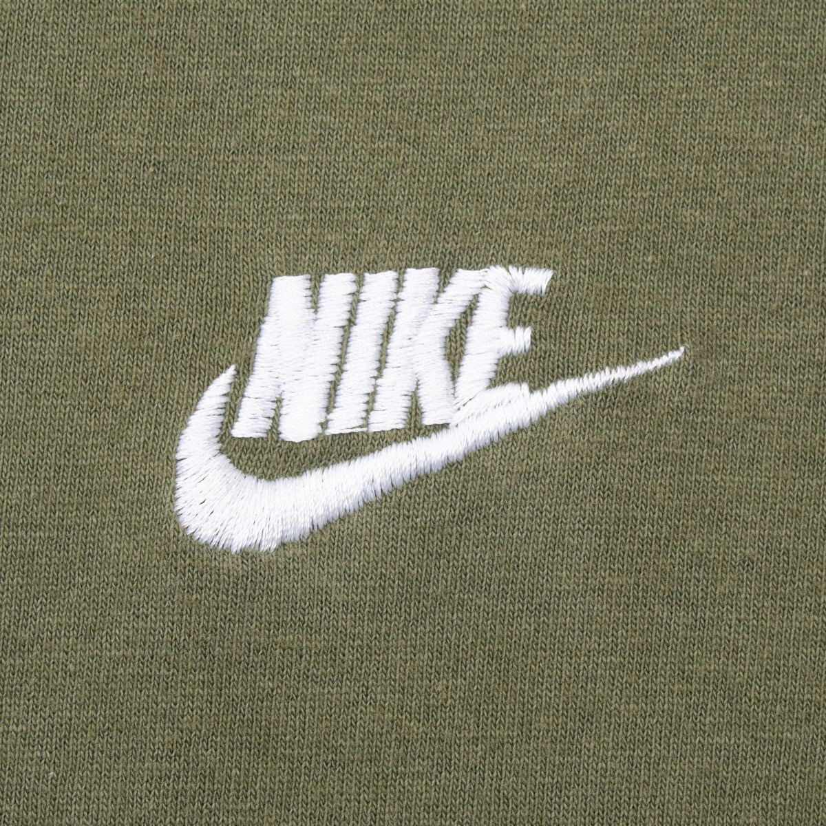Close-up of white embroidered Nike wordmark and Swoosh on olive green fabric
