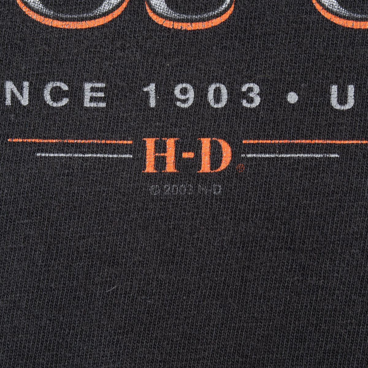 Close-up of orange H-D lettering and gray “Since 1903 USA” print on black fabric