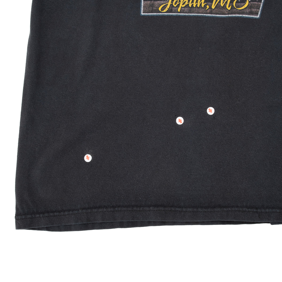 Lower back hem detail of black Harley-Davidson T-shirt showing three small holes