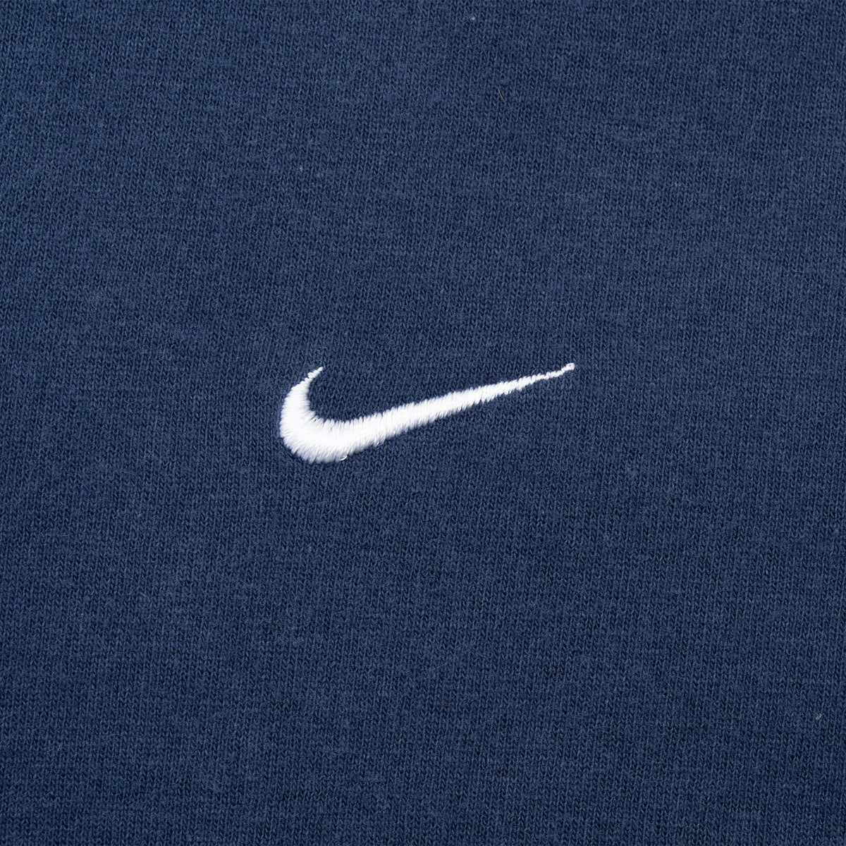 Close-up of small white embroidered Nike Swoosh on navy blue fabric
