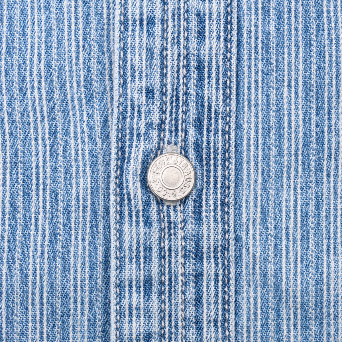 Close-up of engraved Levi Strauss metal button on blue striped fabric