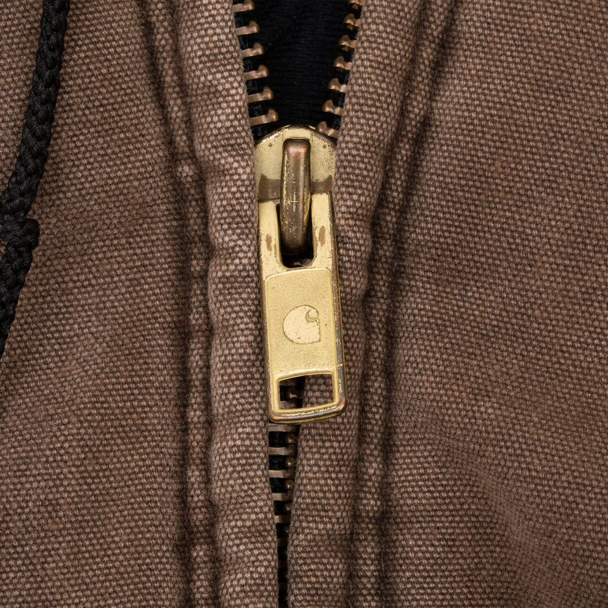 Close-up of Carhartt-branded brass zipper pull on chestnut brown jacket