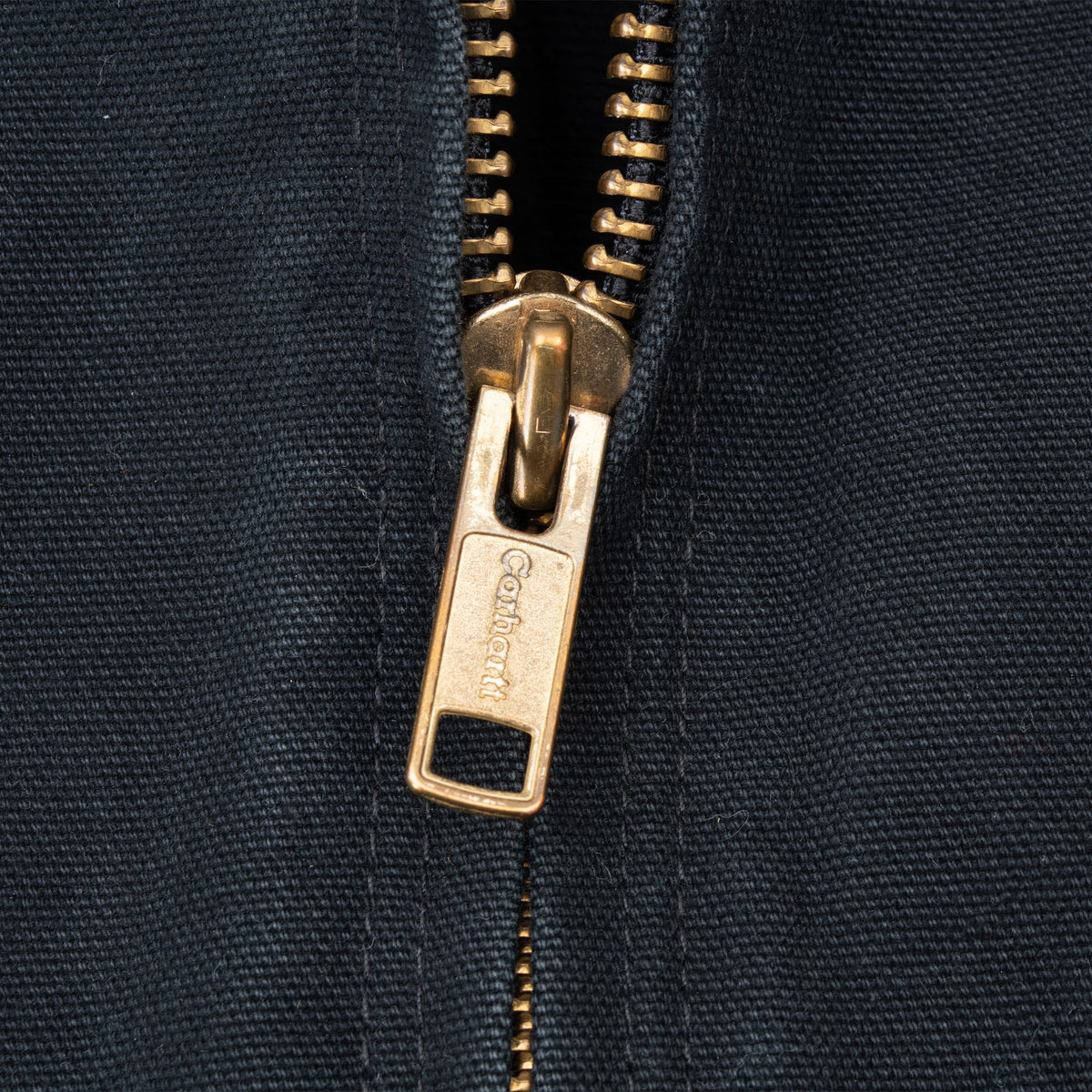 Close-up of brass-tone Carhartt-branded zipper pull on black jacket