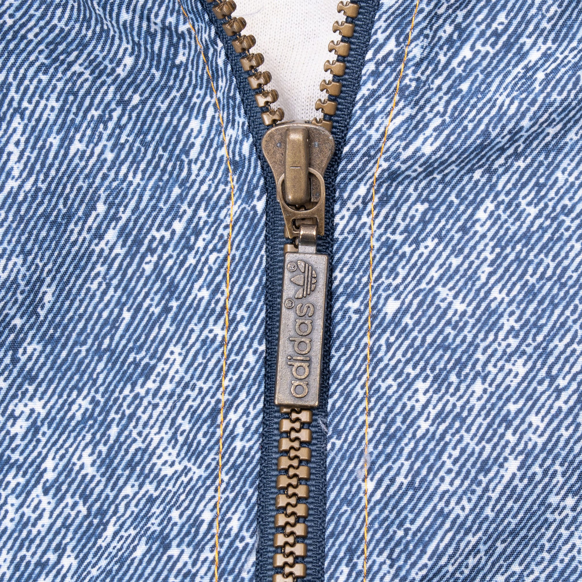 Close-up of adidas-branded metal zipper on blue patterned windbreaker