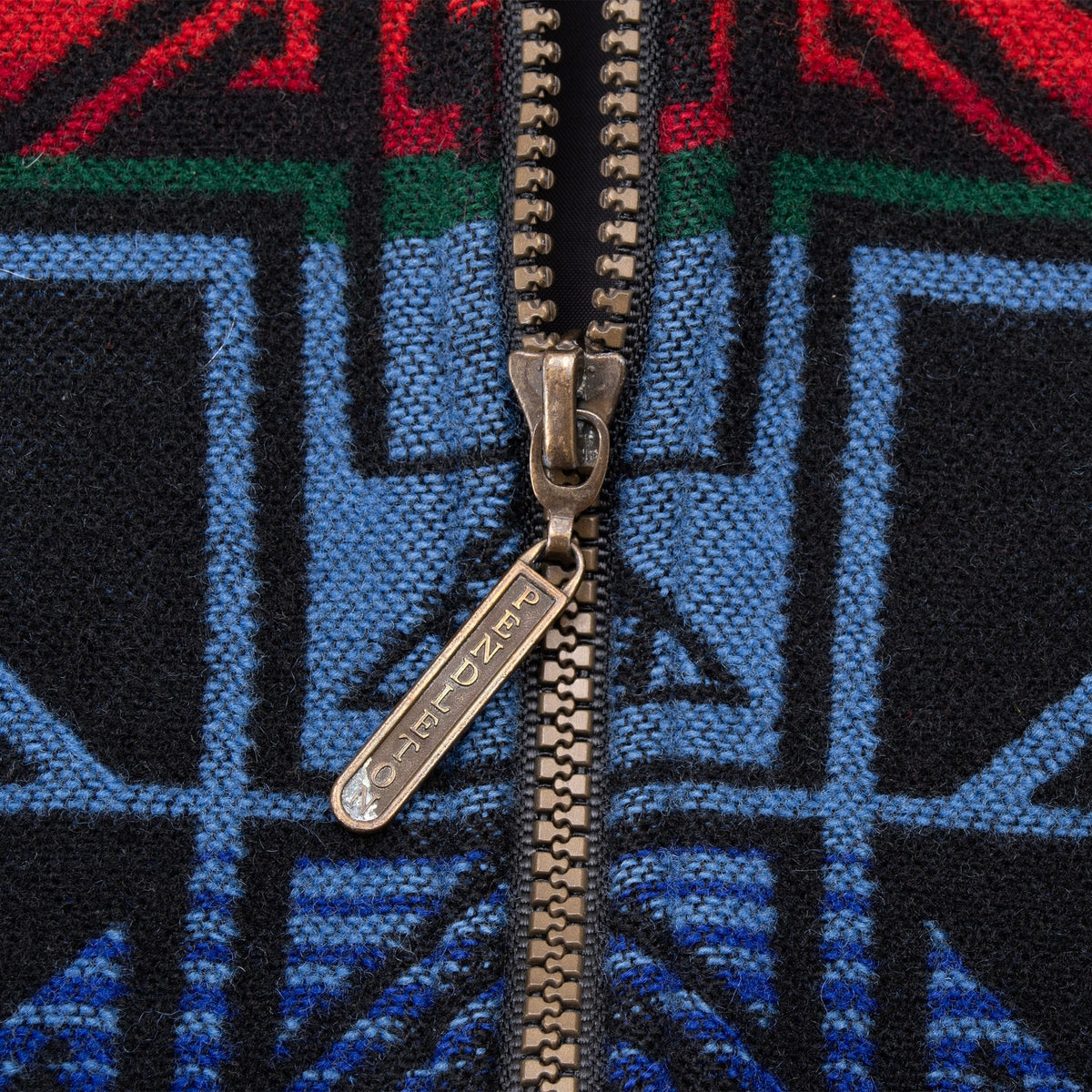 Close-up of Pendleton-branded zipper pull against blue, red and green geometric fabric