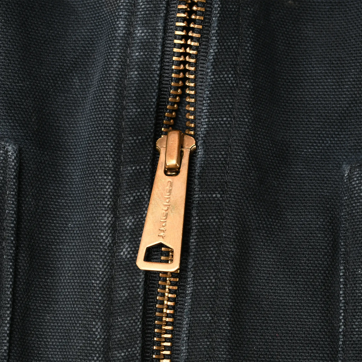 Close-up of brass Carhartt zipper pull against black outer fabric