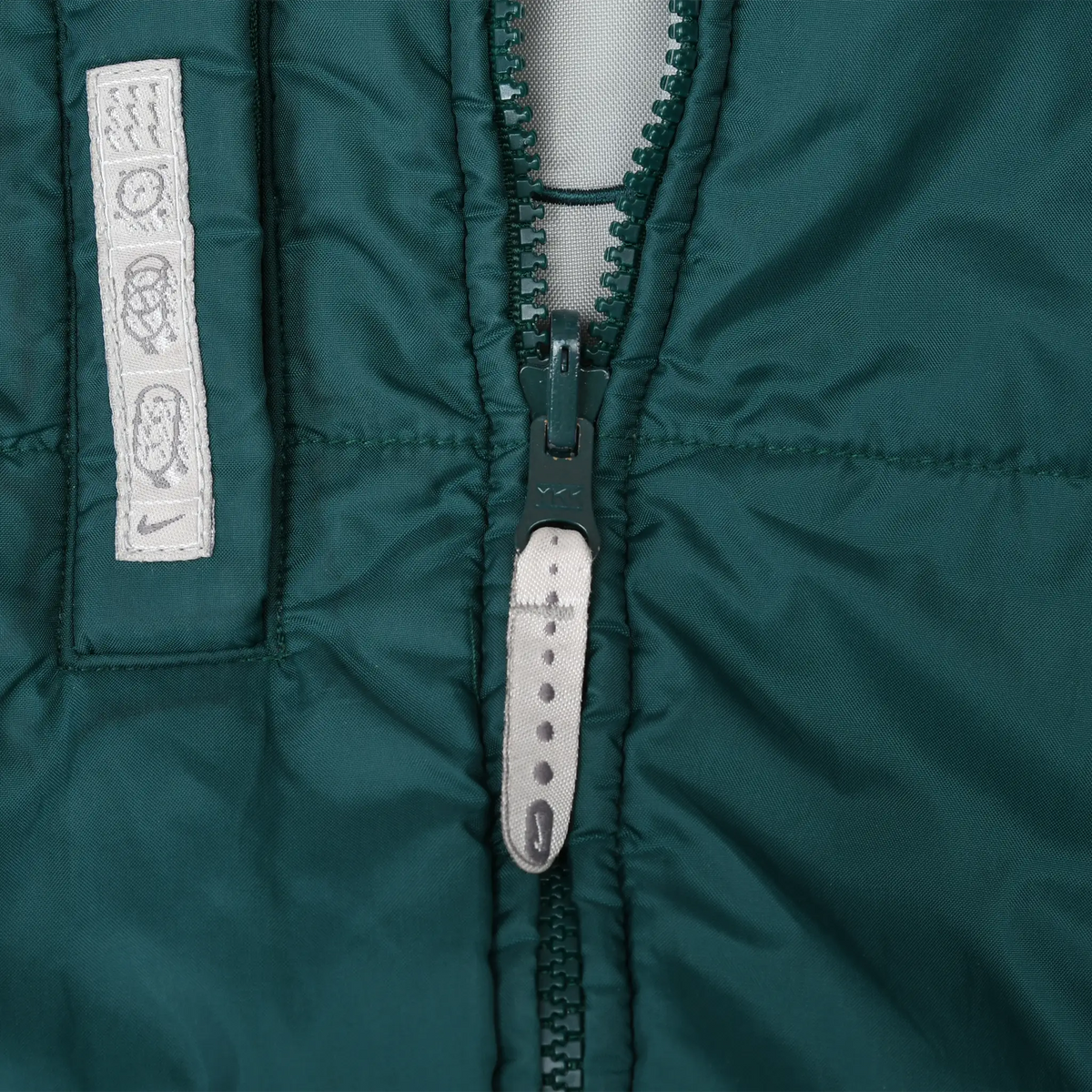 Close-up of green front zipper, grey pull tab, and care symbol label