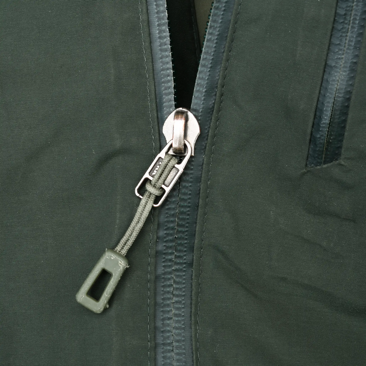 Close-up of main zipper pull and waterproof-sealed seams on green shell jacket