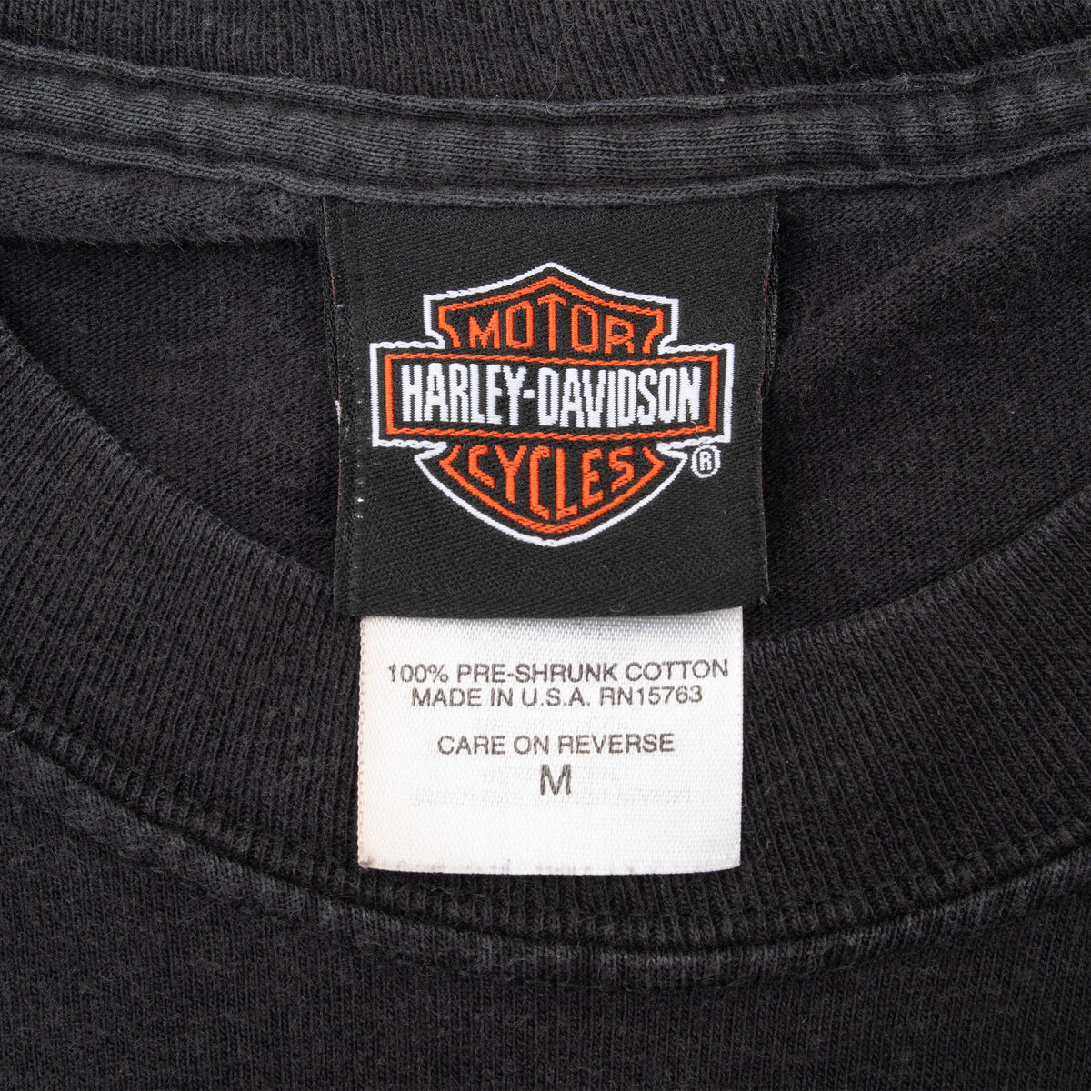 Harley-Davidson neck tag and medium care label on black tee, marked 100% pre-shrunk cotton and made in USA