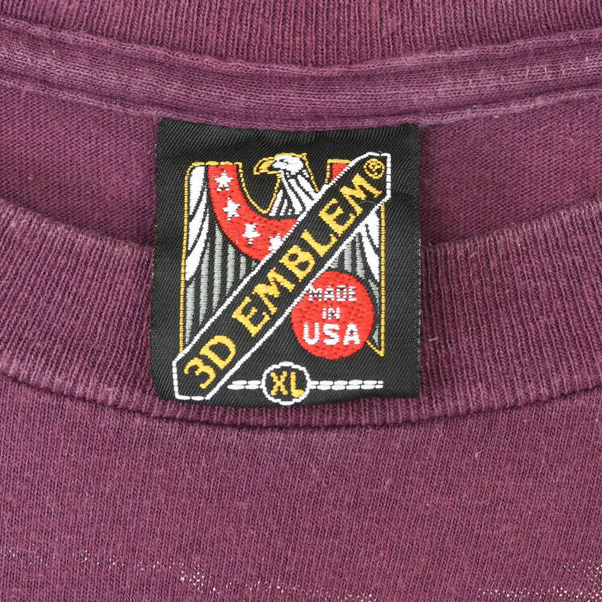 Close-up of 3D Emblem XL Made in USA neck tag on burgundy T-shirt